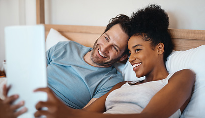 Image showing Happy, relax and carefree interracial couple on digital tablet smiling and taking a selfie in bed. Husband and wife waking up and reading social media news on touchscreen while relaxing at home.