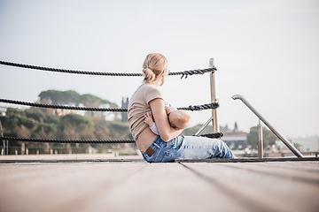 Image showing Mother breast feeding her little baby boy infant child on old wooden pier by the sea on nice warm spring day enjoing nature and warm breeze outdoors.