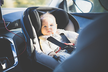 Image showing Cute little baby boy strapped into infant car seat in passenger compartment during car drive.