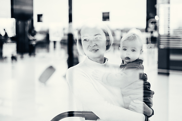 Image showing Thoughtful young mother looking trough window holding his infant baby boy child while waiting to board an airplane at airport terminal departure gates. Travel with baby concept.