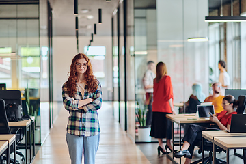 Image showing A portrait of a young businesswoman with modern orange hair captures her poised presence in a hallway of a contemporary startup coworking center, embodying individuality and professional confidence.