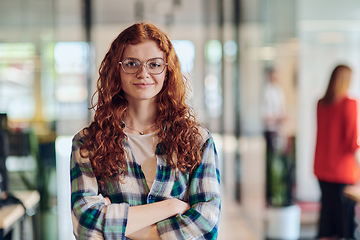Image showing A portrait of a young businesswoman with modern orange hair captures her poised presence in a hallway of a contemporary startup coworking center, embodying individuality and professional confidence.