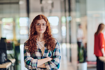 Image showing A portrait of a young businesswoman with modern orange hair captures her poised presence in a hallway of a contemporary startup coworking center, embodying individuality and professional confidence.