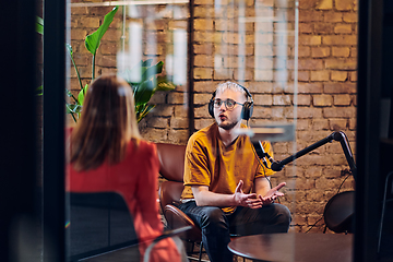 Image showing A gathering of young business professionals, some seated in a glass-walled office, engage in a lively conversation and record an online podcast, embodying modern collaboration and dynamic interaction