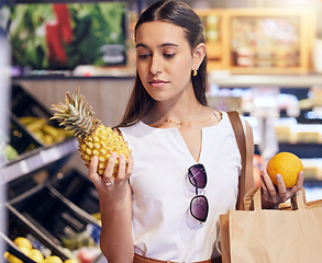Image showing Shopping, holding and looking at fruit at shop, buying healthy food and examining items at a grocery store. Woman deciding, choosing and picking ripe, fresh and delicious produce alone at a market