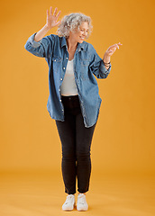Image showing Fun, happy and cheerful woman dancing, celebrating and enjoying life alone against an orange background. Senior woman feeling excited, joyful and playful with dressed stylish, trendy and fashionable
