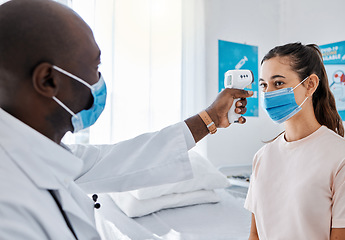 Image showing Covid temperature testing at the hospital by a doctor of a female patient wearing masks and using an infrared thermometer. Medical professional checking a female for covid19 virus or infection