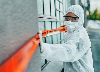 Image showing Covid healthcare worker responding to a biohazard in a public area using barrier tape outside. First responder in protection hazmat suit and mask separating a space due to a new pandemic or outbreak