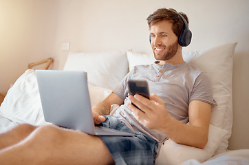 Image showing 5g internet, video and online streaming of a man on a computer and phone in bed. Happy guy with a smile relax and multitask listening to a digital radio podcast or web music with modern technology