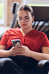 Image showing A businesswoman resting on a short break from work in a modern startup coworking center, using her smartphone to unwind and recharge.