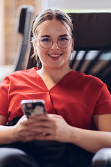 Image showing A businesswoman resting on a short break from work in a modern startup coworking center, using her smartphone to unwind and recharge.