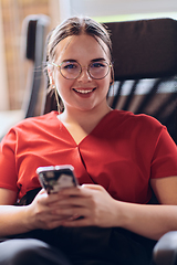 Image showing A businesswoman resting on a short break from work in a modern startup coworking center, using her smartphone to unwind and recharge.