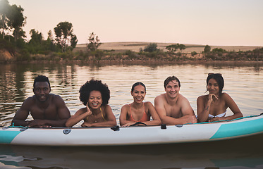 Image showing Diverse group of friends having fun while swimming at a lake in summer with a floating kayak boat. Happy, young and multiracial people on vacation enjoying nature and water on a canoe at sunset.