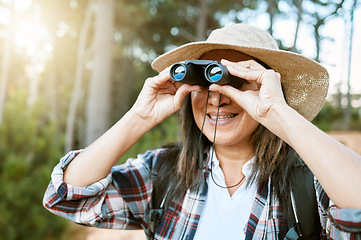 Image showing Female tourist hiking, looking through binoculars at wild birds in the trees. Happy, carefree and mature woman on nature walk, enjoying the view. Outdoor holiday time to promote health and wellness.