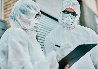 Image showing Healthcare workers wearing protective hazmat suits writing a medical report about covid cases or statistics. First responders filling in a form after doing a safety health check for coronavirus