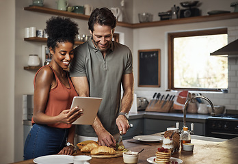 Image showing Young couple cooking healthy food together following recipes online on a tablet, step by step. Happy, cheerful and smiling husband and wife making dinner in the kitchen at home.