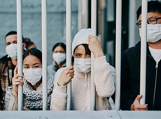 Image showing Foreign people in isolation wearing covid face mask at the border or in quarantine or airport looking unhappy, upset and angry. Poor refugees, immigrants and tourists stuck behind a gate in lockdown
