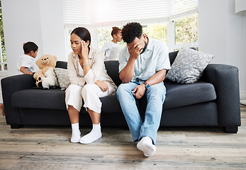 Image showing Sad, unhappy and stressed parents sitting on a couch near their children at home after an argument. Frustrated, tired and annoyed mom and dad are angry at hyperactive, noisy and naughty kids