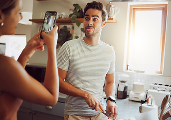 Image showing Silly, goofy and interracial couple taking pictures, having fun and cooking together in the kitchen at home. Happy girlfriend taking pictures of boyfriend, making funny faces and preparing dinner