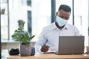 Image showing Covid, mask and business man working in quarantine during a pandemic at the office or workplace for safety. Man alone taking or writing important notes while at work on a laptop and being productive.