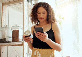 Image showing Female consumer or customer with phone searching organic product information online for ethical, vegan or healthy ingredients. Eco conscious buyer reading label locally made coffee grain jar in store