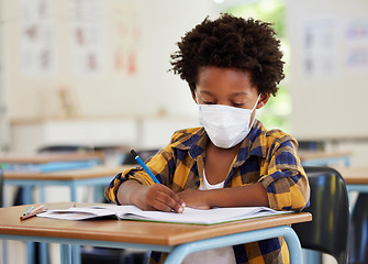 Image showing School boy, student and learning while writing and working in his book inside a classroom with a mask due to covid. Young, serious and African child drawing on paper. Smart kid getting an education