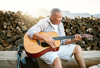 Image showing . Mature man, relaxing and playing the guitar while sitting outdoors and enjoying his hobby while getting fresh air. Older man singing a song in his free time in retirement with a musical instrument.