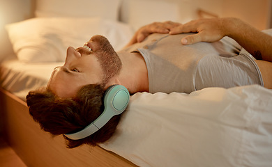 Image showing Happy man, streaming a podcast in bed smiling with headphones at home. Young guy listening to music from spotify on internet or radio in earphones, time to relax, enjoy peace in his apartment bedroom