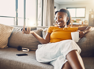 Image showing Relaxed, carefree and smiling young female watching tv and streaming movie at home on her living room sofa. Happy, casual and comfortable woman sitting on her couch and enjoying her leisure free time