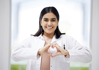 Image showing Smiling, caring medical doctor with heart sign hands gesture in modern clinic or hospital. Happy, positive and wellness young healthcare worker or physician with support and care symbol