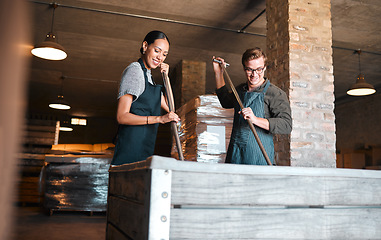 Image showing Wine making, production and cellar workers holding press tool to crush, blend and stir open tank for alcohol process. Vintner, factory and winery industry with distillery and manufacturing warehouse