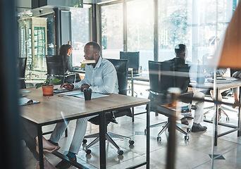 Image showing Business, office and work with a man sitting at his desk in a glass building and working with colleagues in the background. A busy corporate company with an employee and worker at a table for his job