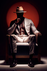 Image showing Silhouette of mysterious man hiding a secret in the dark sitting on a chair against a red light studio background. Trendy, fashion and style African American model wearing a stylish suit