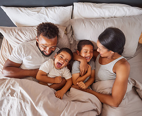 Image showing Happy family bonding in bed together, playing and laughing while being loving and having fun. Young caring interracial parents sharing special moment of parenthood with two playful boys in bedroom