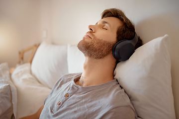 Image showing Relax, meditation and resting man listening to music on his wireless headphones while relaxing on his bed at home. Relaxed and calm male dreaming sleeping due to audiobook or podcast in his bedroom