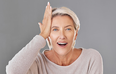 Image showing Thinking, idea or memory with a senior woman knocking her head with her hand to remember or forget in studio on a grey background. Face portrait of a model with grey hair having a light bulb moment