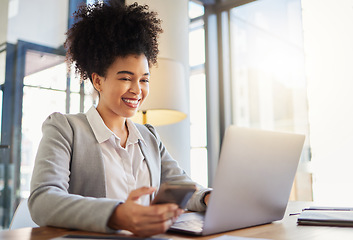 Image showing Happy corporate employee texting on a phone while working on a laptop in an office, reading email. Young professional assistant multitasking to complete an online task, efficient time management