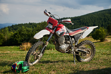 Image showing A professional motocross standing poised in a meadow, fully geared up and ready for a competitive race, with the anticipation of adrenaline-fueled excitement in the air.