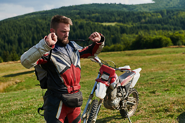 Image showing A professional motocross rider, clad in a full suit, gloves, and backpack, prepares for a daring adventure through the forest, geared up for an adrenaline-pumping off-road journey