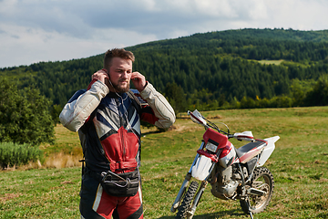 Image showing A professional motocross rider, clad in a full suit, gloves, and backpack, prepares for a daring adventure through the forest, geared up for an adrenaline-pumping off-road journey