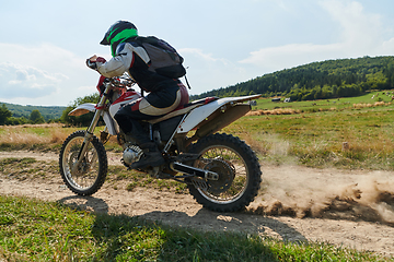 Image showing A professional motocross rider exhilaratingly riding a treacherous off-road forest trail on their motorcycle.