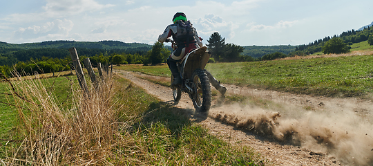 Image showing A professional motocross rider exhilaratingly riding a treacherous off-road forest trail on their motorcycle.