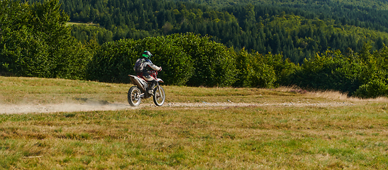 Image showing A professional motocross rider exhilaratingly riding a treacherous off-road forest trail on their motorcycle.