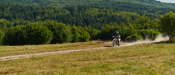 Image showing A professional motocross rider exhilaratingly riding a treacherous off-road forest trail on their motorcycle.