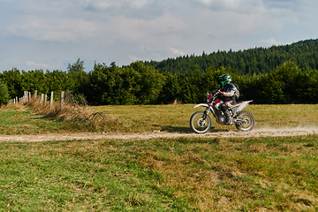 Image showing A professional motocross rider exhilaratingly riding a treacherous off-road forest trail on their motorcycle.