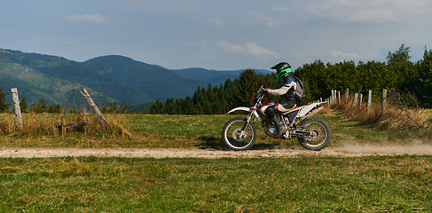 Image showing A professional motocross rider exhilaratingly riding a treacherous off-road forest trail on their motorcycle.