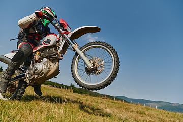 Image showing A fearless professional motocross rider skillfully executes an extreme back wheelie maneuver through a perilous forest terrain, showcasing remarkable balance and daring expertise