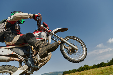 Image showing A fearless professional motocross rider skillfully executes an extreme back wheelie maneuver through a perilous forest terrain, showcasing remarkable balance and daring expertise