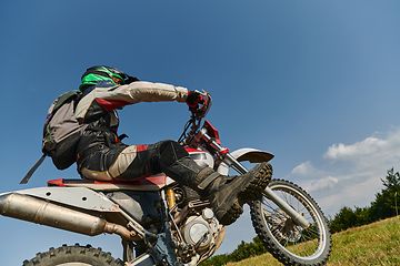 Image showing A fearless professional motocross rider skillfully executes an extreme back wheelie maneuver through a perilous forest terrain, showcasing remarkable balance and daring expertise