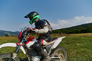 Image showing A motorcyclist equipped with professional gear, rides motocross on perilous meadows, training for an upcoming competition.